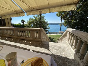 En terrasse med et spisebord, der vender ud mod et vandareal og en fjerntliggende kystlinje.