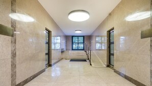 Un corridoio con pareti in marmo, una porta in vetro a fondo e una scala che conduce a un piano superiore.