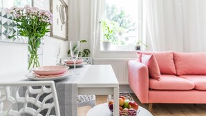 A dining area with a white table, pink plates, a vase of flowers, and a pink sofa. - APT in Alb. nad Orlici by Michal&Friends (Albrechtice nad Orlicí)
