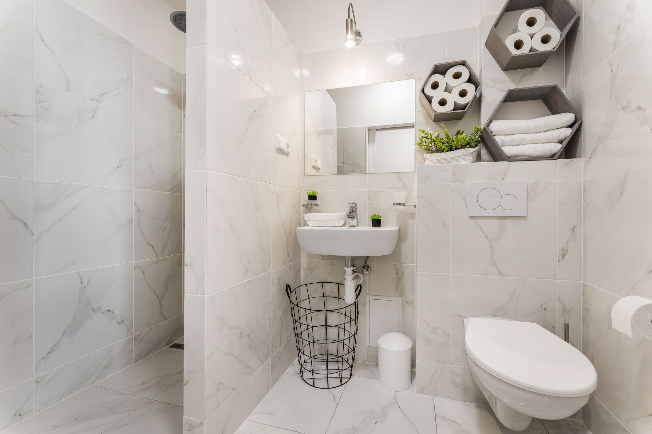A modern bathroom with white marble tiles, a white sink, a toilet, and a shower area.