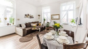 A bright living room with a sofa, dining table set for four, and a large window with sheer curtains. - APT in Alb. nad Orlici by Michal&Friends (Albrechtice nad Orlicí)
