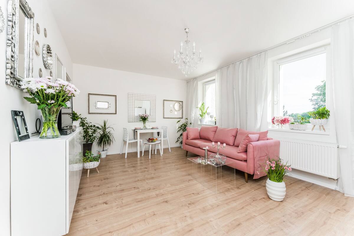 Ett modernt vardagsrum med en rosa soffa, ett vitt soffbord och en matplats med ett vitt bord och stolar.