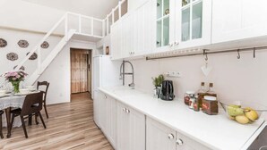 A modern kitchen with white cabinets, a wooden staircase, and a dining area with a table set for two. - APT in Alb. nad Orlici by Michal&Friends (Albrechtice nad Orlicí)