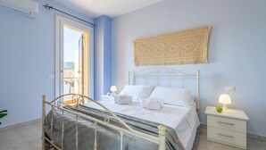 A bedroom with a bed, bedside table, lamp, and a view through an open door. - Holiday Home "Junco" with Garden, Loggia and Wi-Fi (Villasimius)