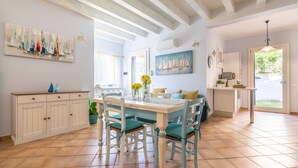 A dining area with a white table, teal chairs, and a kitchen in the background. - Holiday Home "Alloggio Nettuno" with Garden, Loggia and Wi-Fi (Villasimius)
