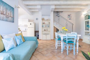 A living room with a sofa, a dining table with chairs, a staircase, and a kitchen area.