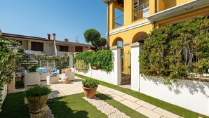 A courtyard with a white wall, a yellow building, and potted plants. - Holiday Home "Alloggio Nettuno" with Garden, Loggia and Wi-Fi (Villasimius)