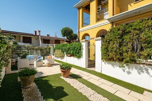 A courtyard with a white wall, a yellow building, and potted plants.