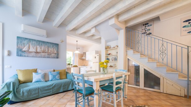 A spacious living area with a sofa, dining table, chairs, and a staircase. - Holiday Home "Alloggio Nettuno" with Garden, Loggia and Wi-Fi (Villasimius)