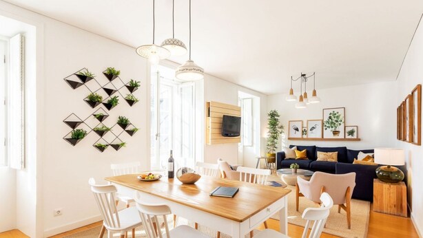 A modern living space with a dining area, a sofa, and a TV mounted on the wall. - JOIVY Chiado Self Check-In 2-BR Flat w/Parking (Lisbon)