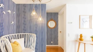 A room with a white wicker sofa, a round mirror, and a wooden table with a yellow vase. - JOIVY Chiado Self Check-In 2-BR Flat w/Parking (Lisbon)