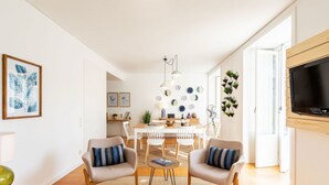 A modern living room with a dining area, featuring a sofa set, a coffee table, and a TV mounted on the wall. - JOIVY Chiado Self Check-In 2-BR Flat w/Parking (Lisbon)
