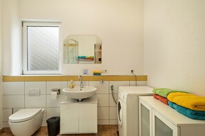 A bathroom with a toilet, sink, mirror, window, and washing machine. - Stylish Holiday Apartment "Tuna" in Old Building Villa, with Mountain View (Sigmarszell)