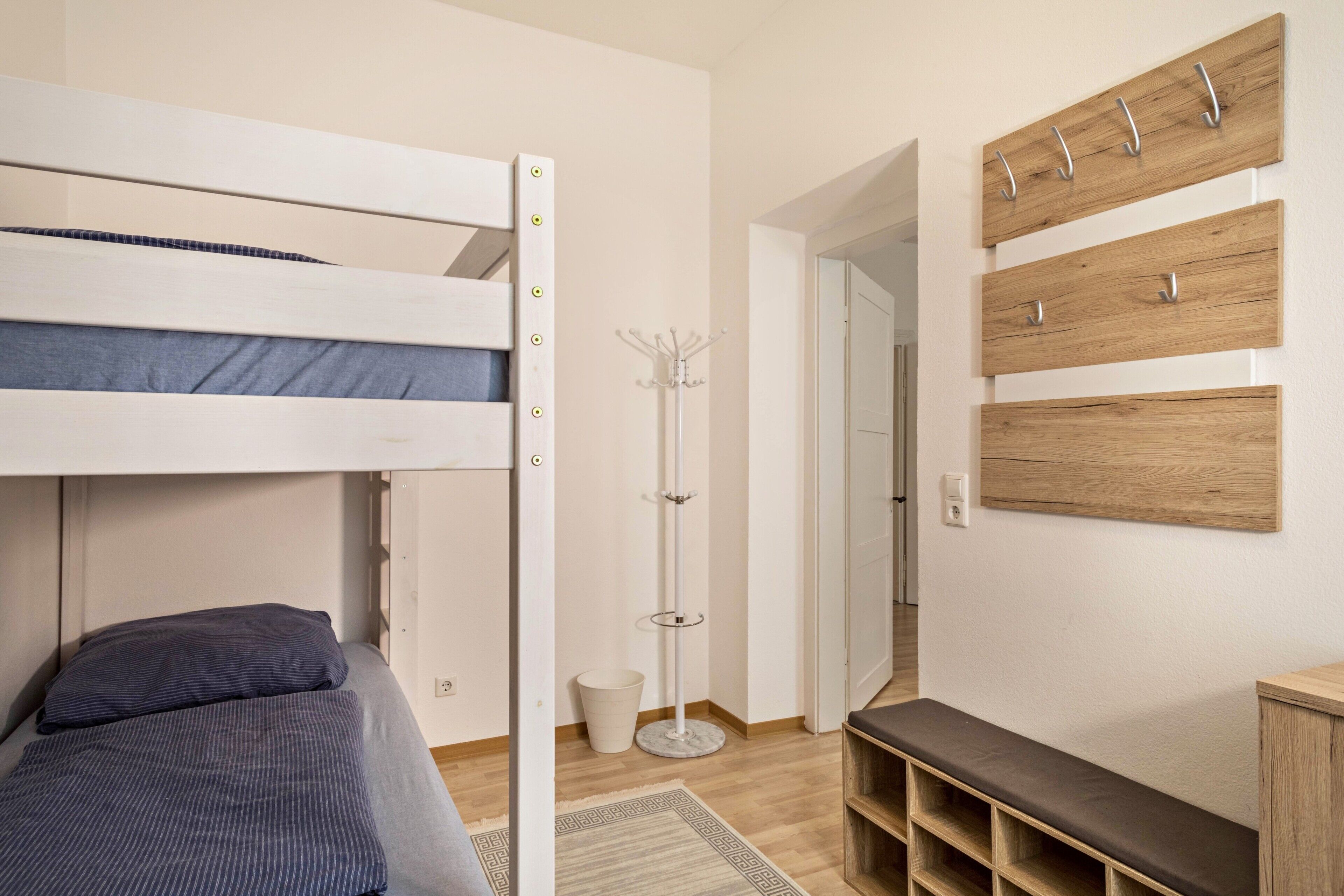 A bunk bed with a bedside table, a coat rack, a bench, and a small shelf unit.