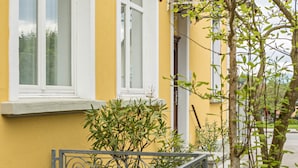 Un bâtiment jaune avec des fenêtres à encadrement blanc, un portail en métal et un arbre au premier plan.