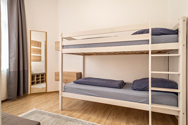 A bunk bed with grey bedding, a wooden floor, a mirror, and a wardrobe.