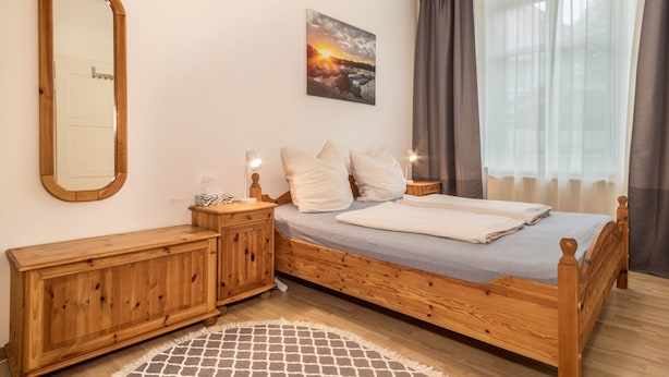 Une chambre à coucher avec un lit en bois, une table de chevet, un miroir, un tableau et une fenêtre avec des rideaux.