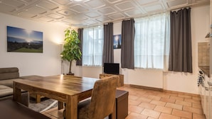 Un espace repas comprenant une table en bois, des chaises, un canapé, un téléviseur et une plante.