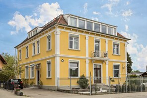 A yellow building with multiple windows, a balcony, and a gated entrance. - Stylish Holiday Apartment "Tuna" in Old Building Villa, with Mountain View (Sigmarszell)