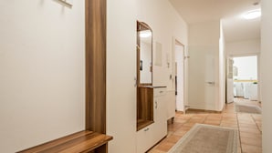 Un couloir avec un banc en bois, un miroir, une porte et un sol carrelé.