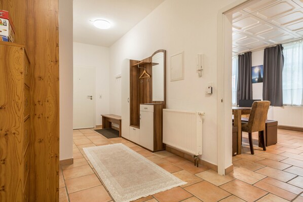 Una habitación con un armario de madera, un radiador blanco, una puerta de madera, un banco y un comedor con una silla.