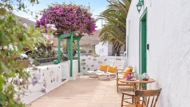 A patio with outdoor furniture, a hanging flower arrangement, and a white building with green accents. - Rustic Holiday Home "Casa Rural Tamia" with Terrace and Mountain View, Wi-Fi (Tao)