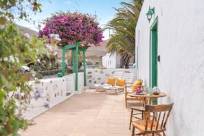 A patio with outdoor furniture, a hanging flower arrangement, and a white building with green accents. - Rustic Holiday Home "Casa Rural Tamia" with Terrace and Mountain View, Wi-Fi (Tao)