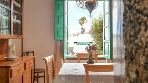 A room with a dining table, chairs, a cabinet, and an open window with a view of greenery and a white building. - Rustic Holiday Home "Casa Rural Tamia" with Terrace and Mountain View, Wi-Fi (Tao)