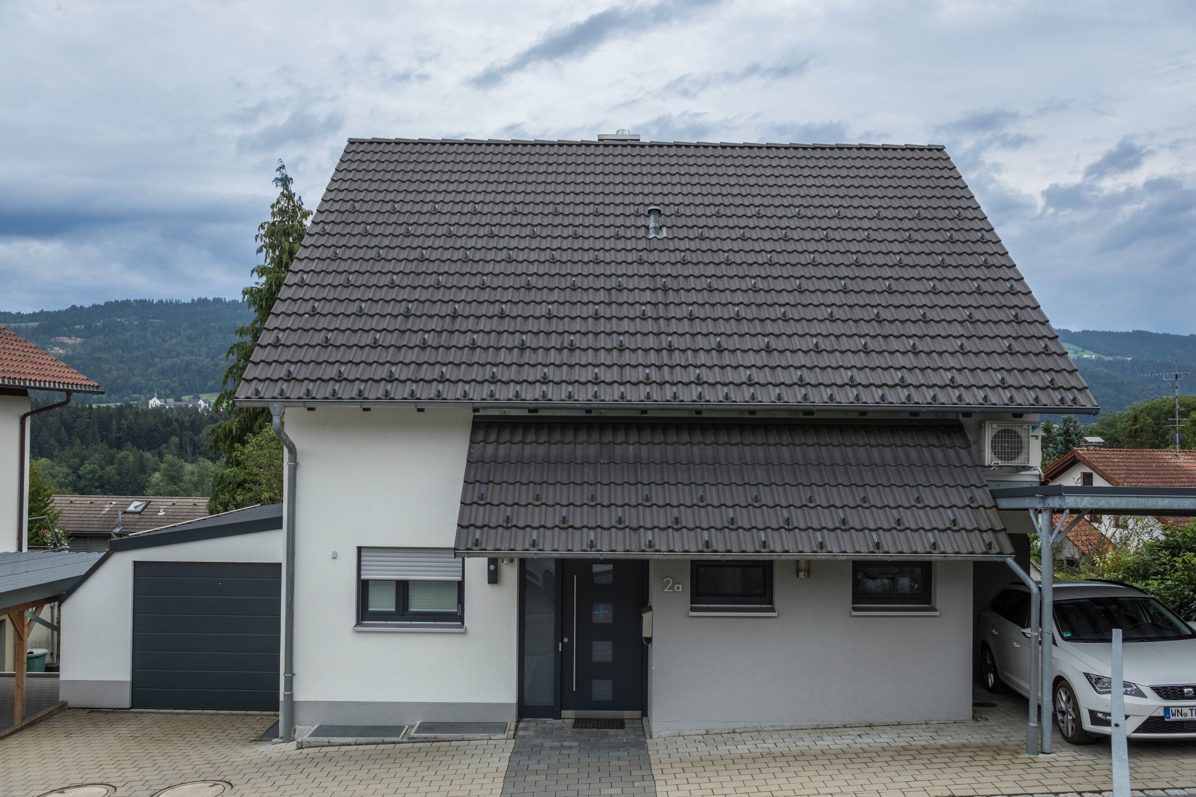A two-story house with a tiled roof, a garage, and a car parked in the driveway.