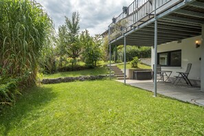 Une maison moderne dotée d’un patio couvert, d’un mur de soutènement en pierre et d’un jardin verdoyant.