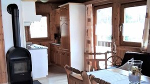 A cozy cabin interior with a wood-burning stove, a dining area with wooden chairs, and a kitchen with wooden cabinets. - Gerda's Ferienhäuser (Eppenschlag)