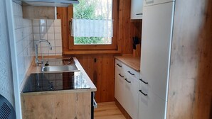 A compact kitchen with wooden cabinets, a stainless steel sink, and a window with a view of greenery. - Gerda's Ferienhäuser (Eppenschlag)