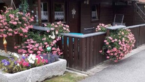 A wooden cabin with a tiled roof, surrounded by flower beds with pink and purple flowers. - Gerda's Ferienhäuser (Eppenschlag)