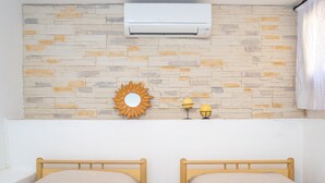 A bedroom with two wooden beds, a stone-patterned wall, an air conditioner, a sun-shaped decoration, and a small table with a lamp. - Holiday Home "Appartamento del Cormorano" Near the Beach and with & Air Conditioning (OLBIA)