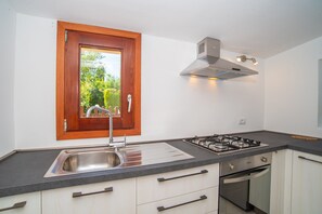 Une cuisine avec une fenêtre, un évier en acier inoxydable, une cuisinière à gaz, un four et des armoires blanches.