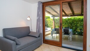 A room with a grey sofa, a floor lamp, and a sliding glass door leading to an outdoor patio with a table and chairs. - Holiday Home "Appartamento del Cormorano" Near the Beach and with & Air Conditioning (OLBIA)