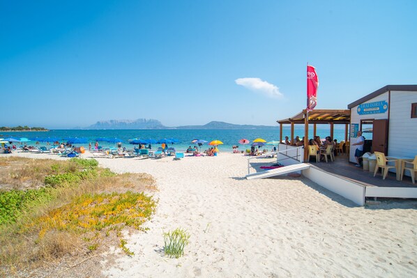 Un bar situé en bord de mer, avec des tables à l’extérieur, un drapeau et une vue sur l’océan.