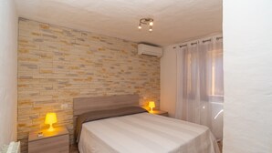 Une chambre avec un mur décoré d’un motif en briques, un lit avec une tête de lit, deux lampes de chevet et un appareil de climatisation.