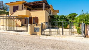 Une maison à deux étages, dotée d’une entrée fermée par un portail, d’un patio couvert et d’un petit escalier menant à l’entrée.
