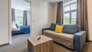 Habitació moderna amb sofà, taula de fusta petita i finestra amb cortines.