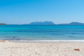 Una spiaggia con acqua turchese cristallina, una barca a vela e montagne sullo sfondo.