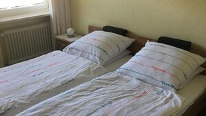 A double bed with white bedding and multiple pillows, a bedside table with a lamp, and a framed floral painting on the wall. - Gästehaus Erna Meier (Bayerisch Eisenstein)
