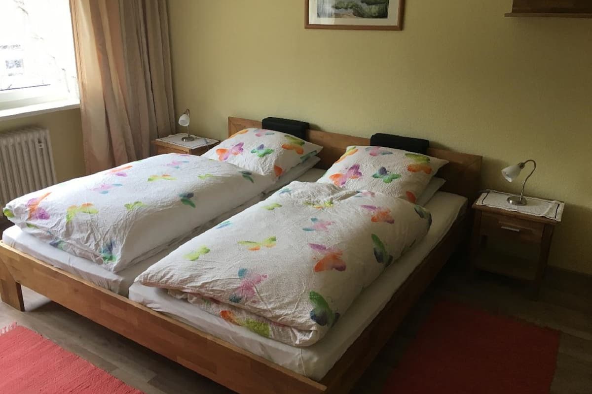 Una cama doble con ropa de cama floral, dos mesitas de noche, una lámpara y un cuadro en la pared.