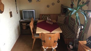 A cozy room with a wooden dining table, a television, a sofa, and a potted plant. - Gästehaus Erna Meier (Bayerisch Eisenstein)