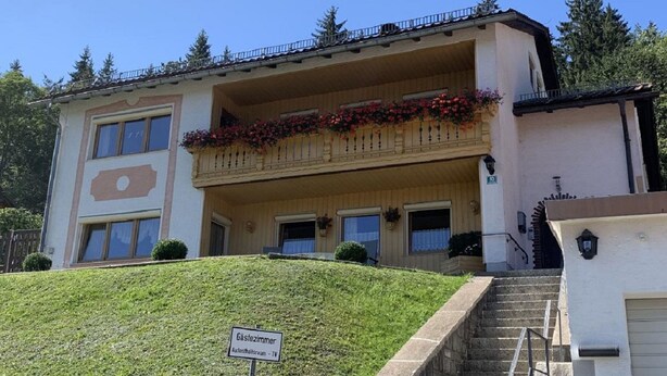 A two-story building with a balcony adorned with red flowers, a sign indicating it is a guesthouse, and a staircase leading to the entrance. - Gästehaus Erna Meier (Bayerisch Eisenstein)
