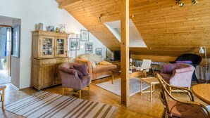 A cozy loft-style room with a high wooden ceiling, a sofa, armchairs, a dining table, and a cabinet with glass doors. - Holiday Apartment “Rose Garden” near Lake Constance with Wi-Fi & Balcony (Heiligenberg)