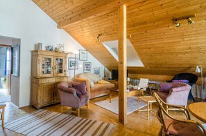 Une pièce confortable de style loft, avec un haut plafond en bois, un canapé, des fauteuils, une table à manger et un meuble avec des portes en verre.