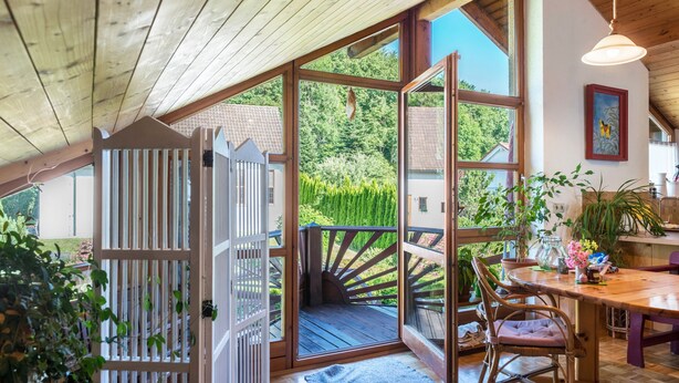 A wooden deck with a glass door leading to a balcony, a dining table with chairs, and a hanging light fixture. - Holiday Apartment “Rose Garden” near Lake Constance with Wi-Fi & Balcony (Heiligenberg)