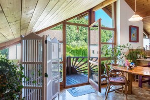 A wooden deck with a glass door leading to a balcony, a dining table with chairs, and a hanging light fixture.