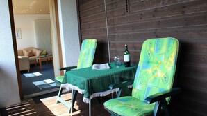 A patio area with two green chairs and a table covered with a green tablecloth. A bottle of wine and a glass are on the table.